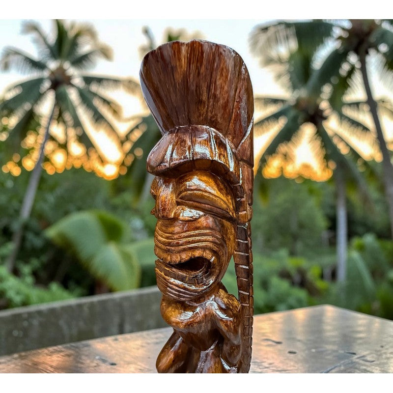 Carved wooden tiki figure on a table with blurred tropical background