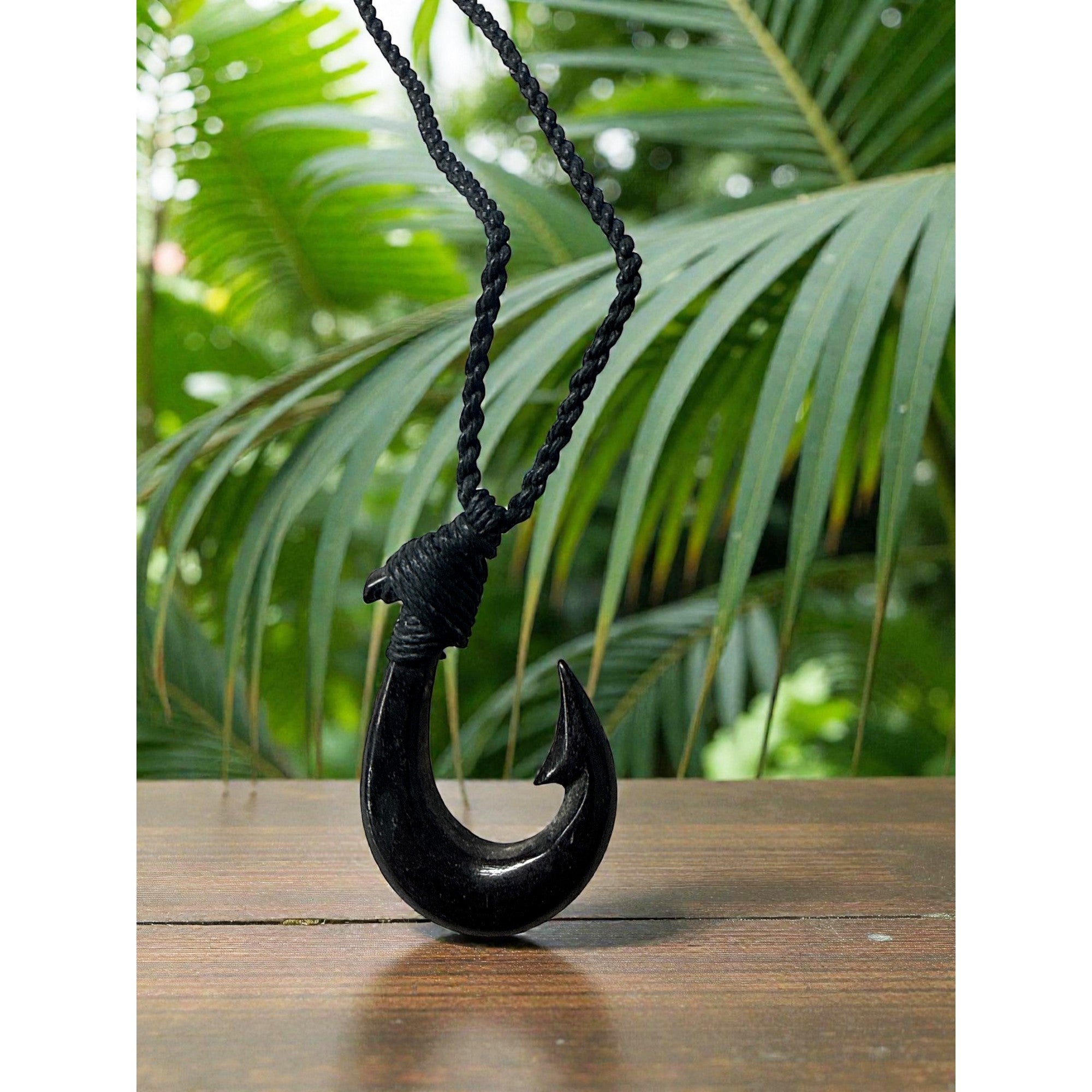 Black fish hook pendant on a rope against a green leafy background