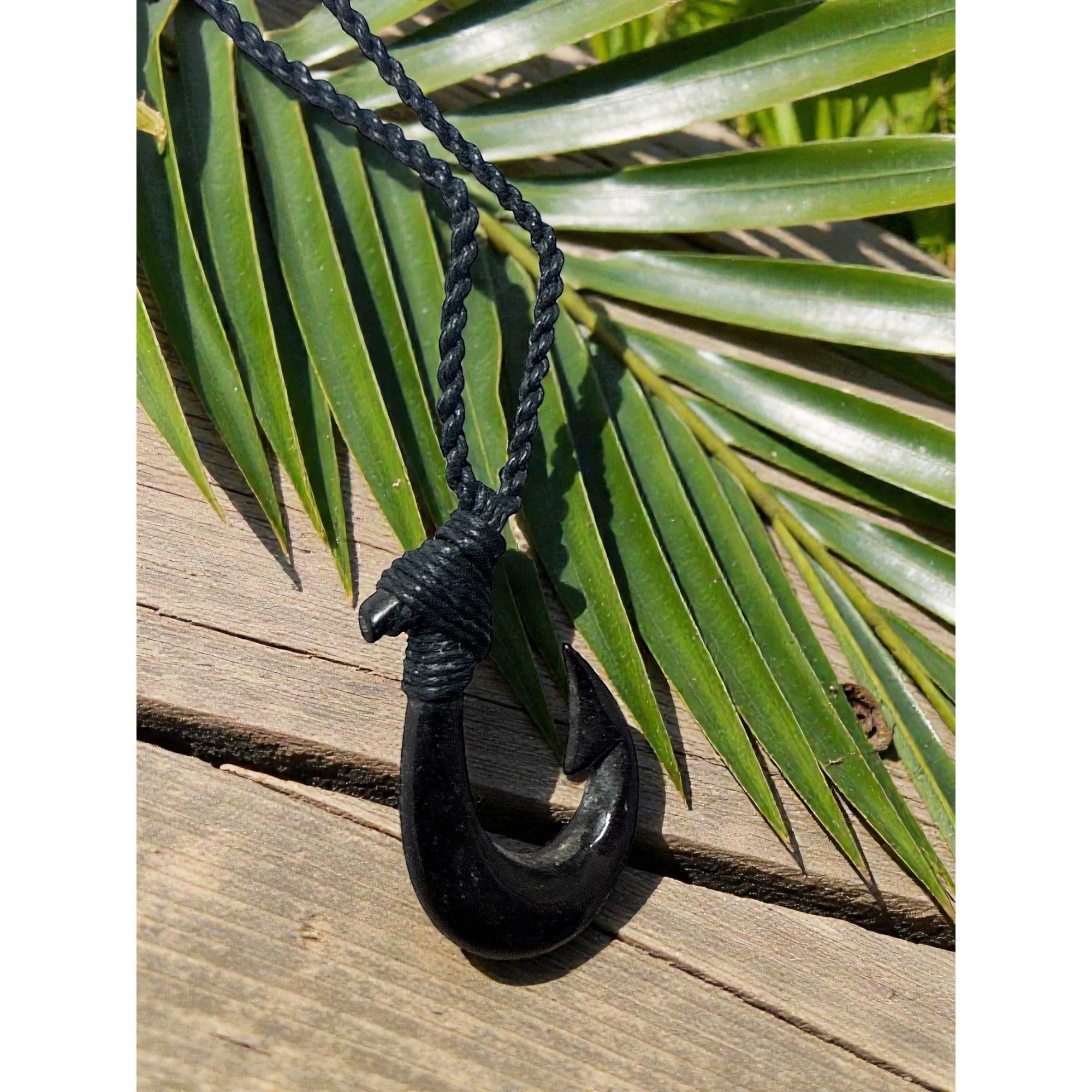 Black hook pendant on a rope against a background of green palm leaves.