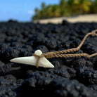 Shark tooth necklace on black volcanic rock with blurred greenery in the background