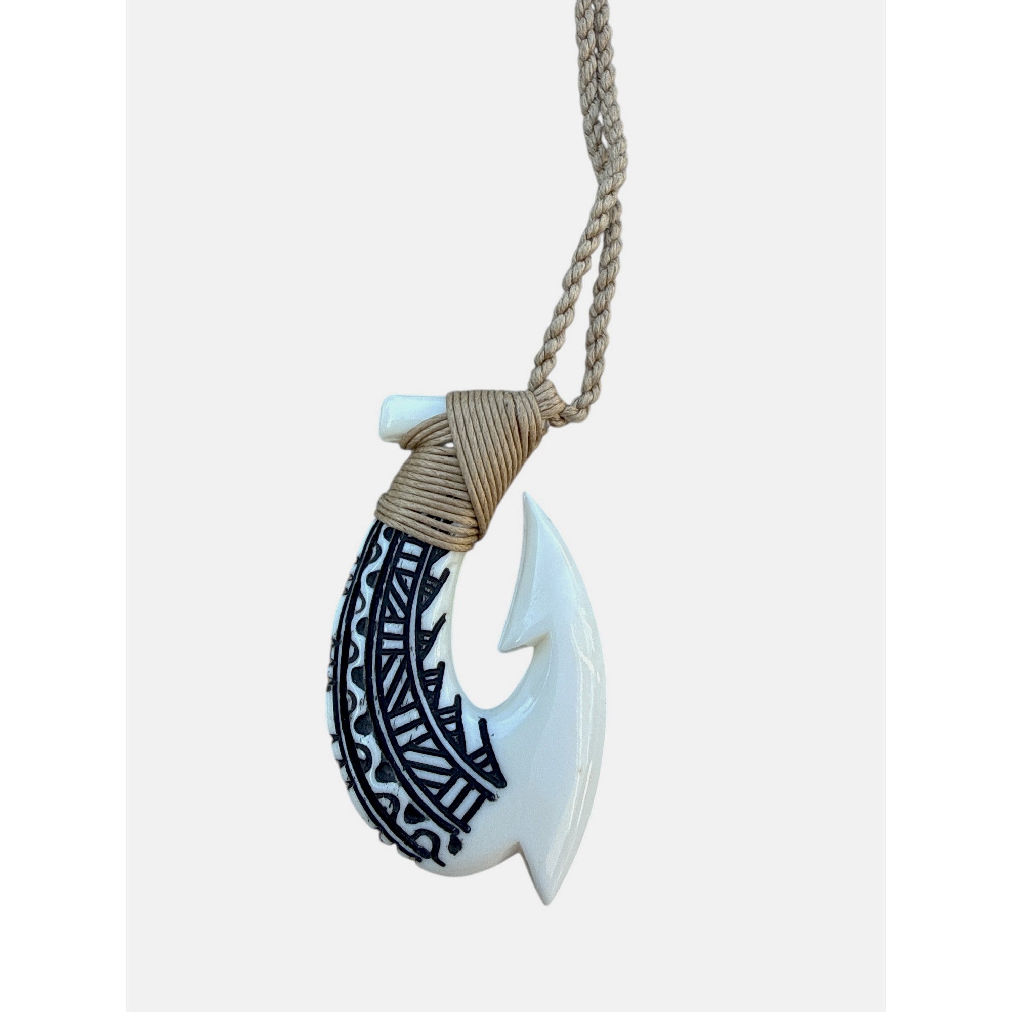 White fish hook pendant with black patterns on a beige cord against a white background