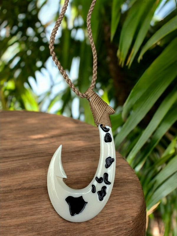White fish hook pendant with black patterns on a brown surface, palm leaves in the background