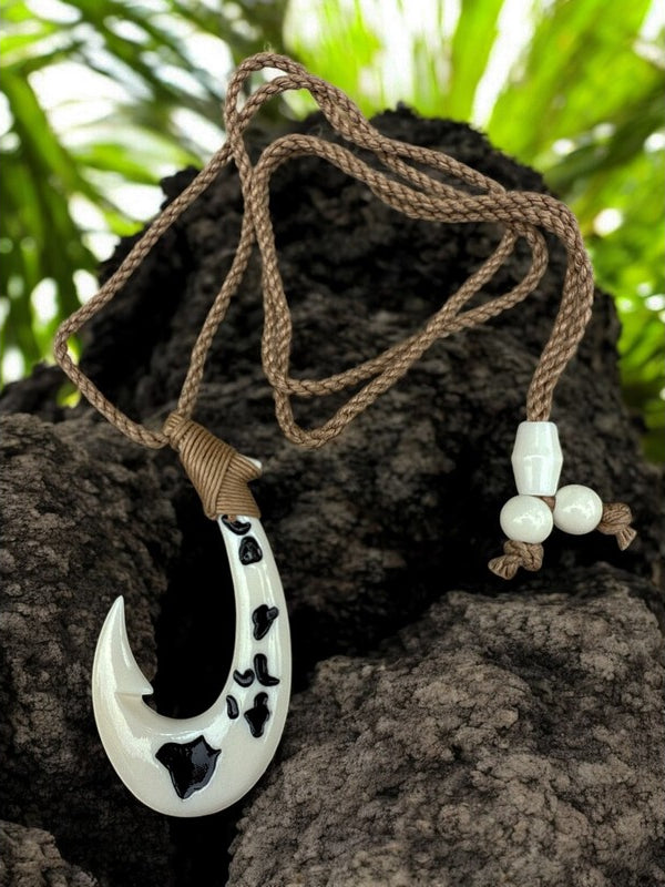 White fish hook pendant with black patterns on a brown rope, set against a natural background.