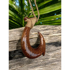 Wooden fish hook pendant on a rope against a wooden background with greenery.