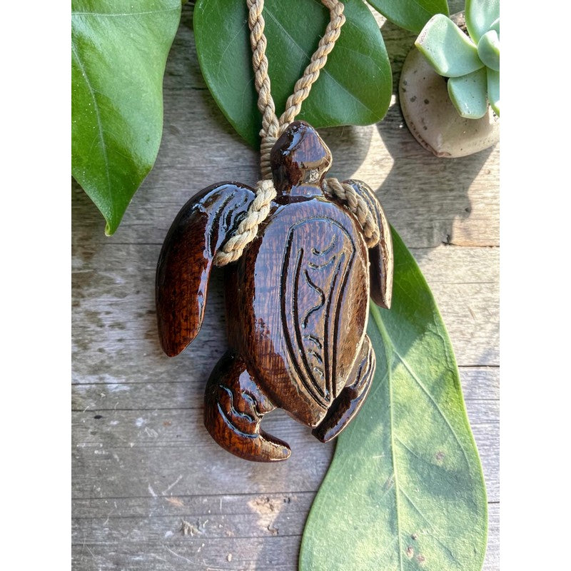 Wooden turtle pendant on a rope with green leaves in the background