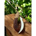 Wooden pendant with white blade on a rope, set against a natural background