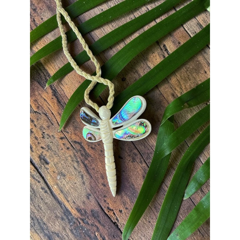 Dragonfly-shaped pendant on a cord with green leaves on a wooden surface