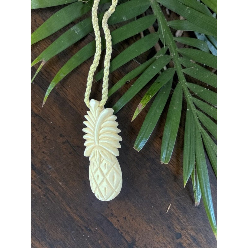 Carved pineapple pendant on a string with green leaves in the background