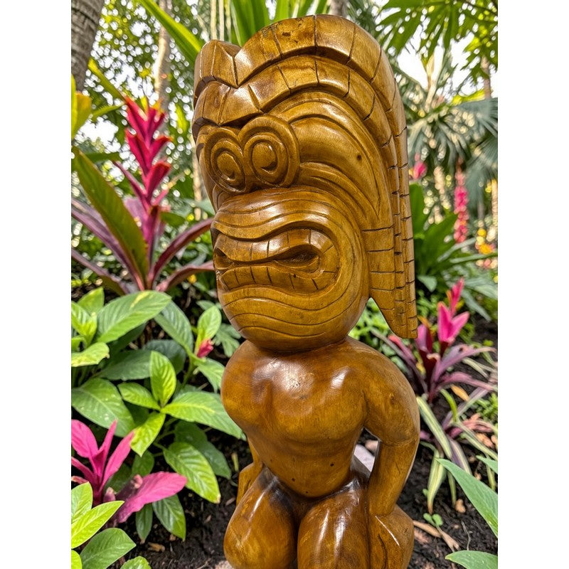 Wooden tiki statue in a garden setting with plants and flowers.