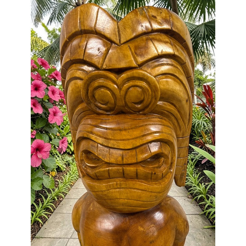 Wooden tiki mask statue in a garden setting with flowers and plants.