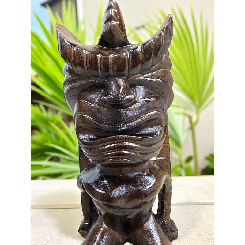Carved wooden tiki statue with a blurred green plant background