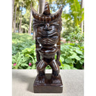 Wooden tiki statue on a stone surface with a garden background