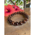 Brown beaded bracelet on a wooden surface with pink flowers in the background