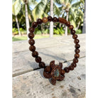 Brown beaded bracelet with a decorative clasp on a wooden surface with palm trees in the background