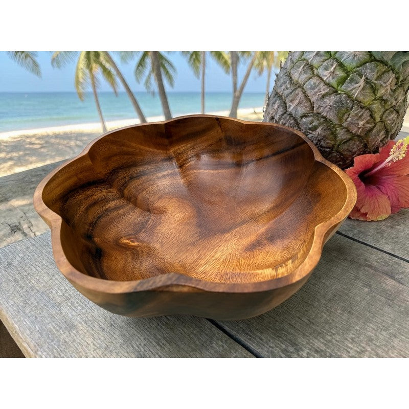 Wooden bowl on a wooden surface with a pineapple and hibiscus flower in the background.