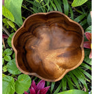 Wooden bowl with a natural finish surrounded by green foliage and a pink flower.