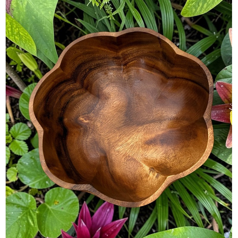Wooden bowl with a natural finish surrounded by green foliage and a pink flower.