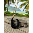 Black fish hook pendant on a wooden surface with a tropical beach background