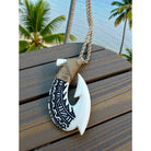Necklace with fish hook pendant on a wooden surface with palm trees in the background
