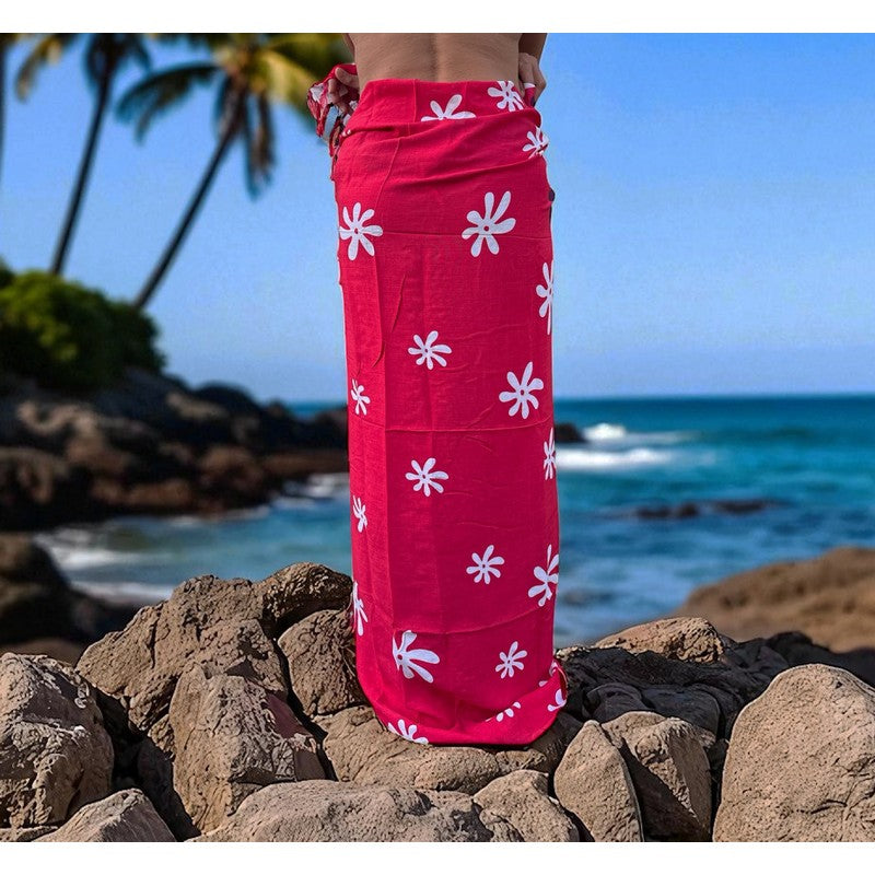 Person wearing a pink floral sarong standing on rocks with ocean and palm trees in the background