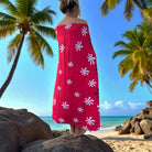 Person wearing a red floral towel on a tropical beach with palm trees and clear blue sky.