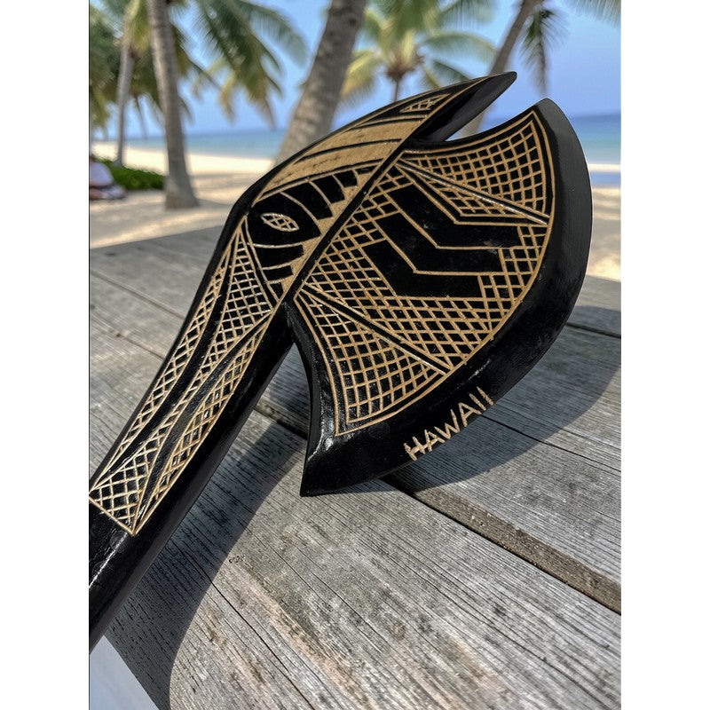 Black and gold paddle with 'Hawaii' branding on a wooden surface with palm trees in the background