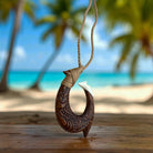 Wooden fish hook pendant on a rope with a beach background