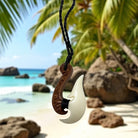Hook-shaped necklace with carvings on a tropical beach with palm trees and ocean.