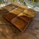 A rectangular wooden serving tray with four compartments, placed on a rustic wooden table with natural outdoor light and palm leaves in the background.