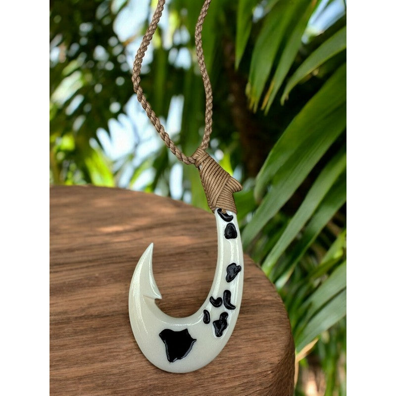 White fish hook pendant with black patterns on a brown surface, palm leaves in the background