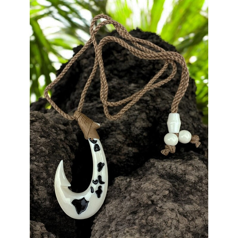 White fish hook pendant with black patterns on a brown rope, set against a natural background.