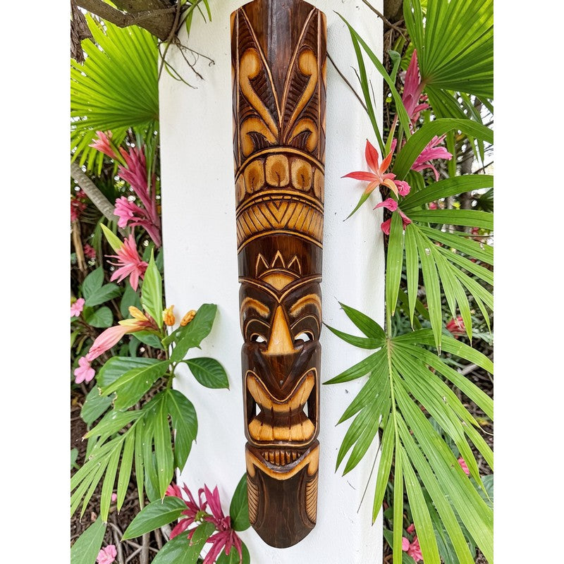 Wooden tiki mask with tropical plants and flowers in the background