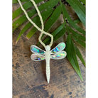 Dragonfly-shaped pendant on a cord with green leaves in the background