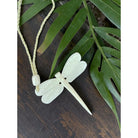Dragonfly-shaped pendant on a cord with green leaves in the background