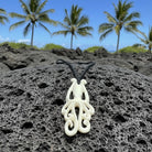 White octopus-shaped necklace on black volcanic rock with palm trees in the background