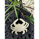 White crab pendant on a black cord against a natural background