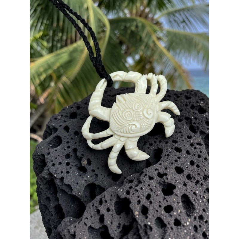 Carved crab pendant on a black stone with palm leaves in the background