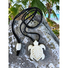 Turtle-shaped pendant on a black cord with a tropical background