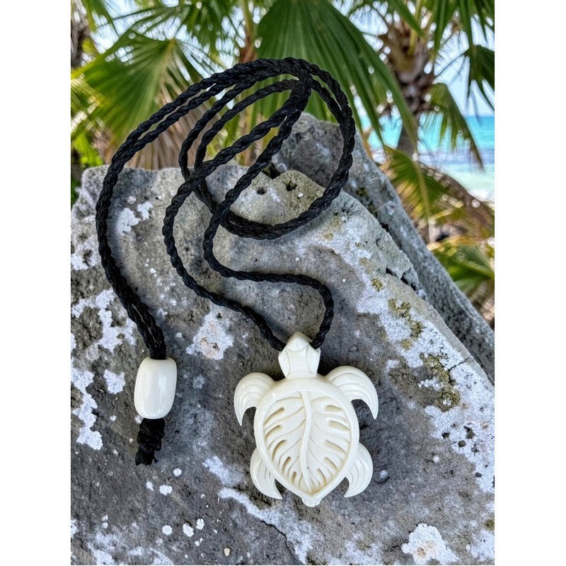 Turtle-shaped pendant on a black cord with a tropical background