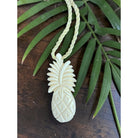 White pineapple-shaped pendant on a green cord with a leafy background