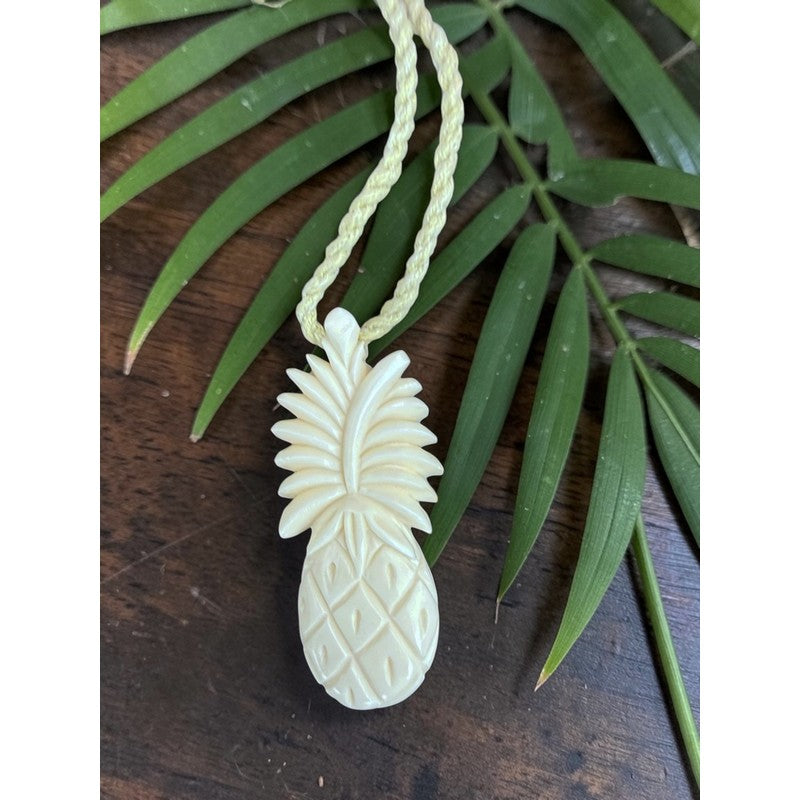 White pineapple-shaped pendant on a green cord with a leafy background