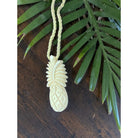 Carved pineapple pendant on a string with green leaves in the background