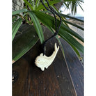 White fish-shaped hook on a wooden surface with green leaves in the background