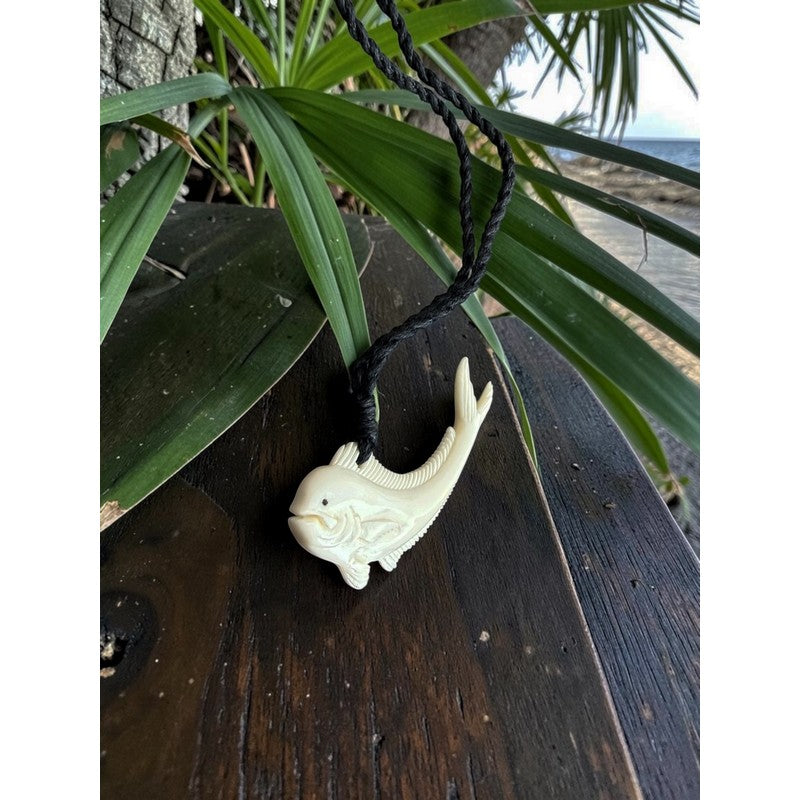 White fish-shaped hook on a wooden surface with green leaves in the background