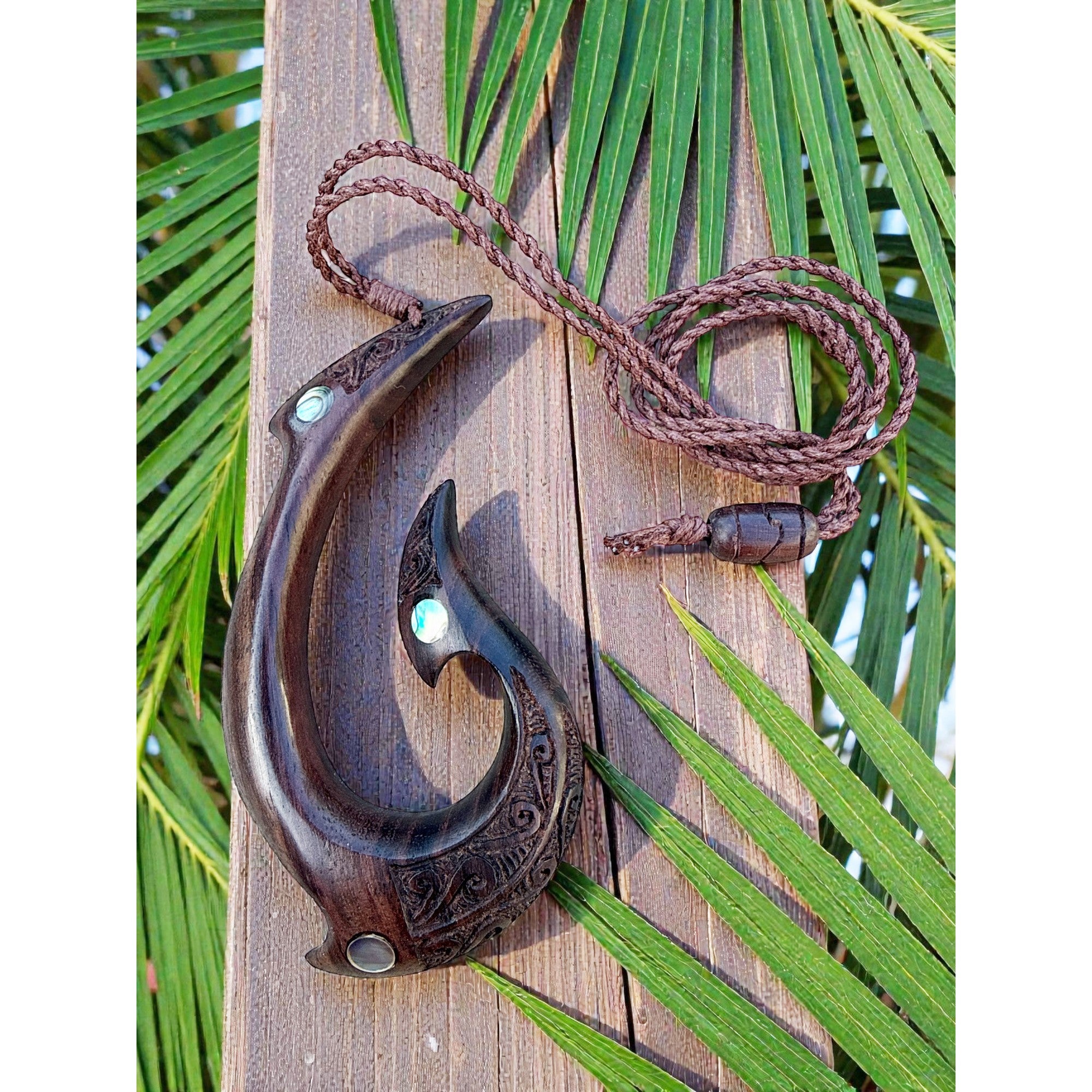 Wooden fish hook pendant on a wooden board with green leaves in the background