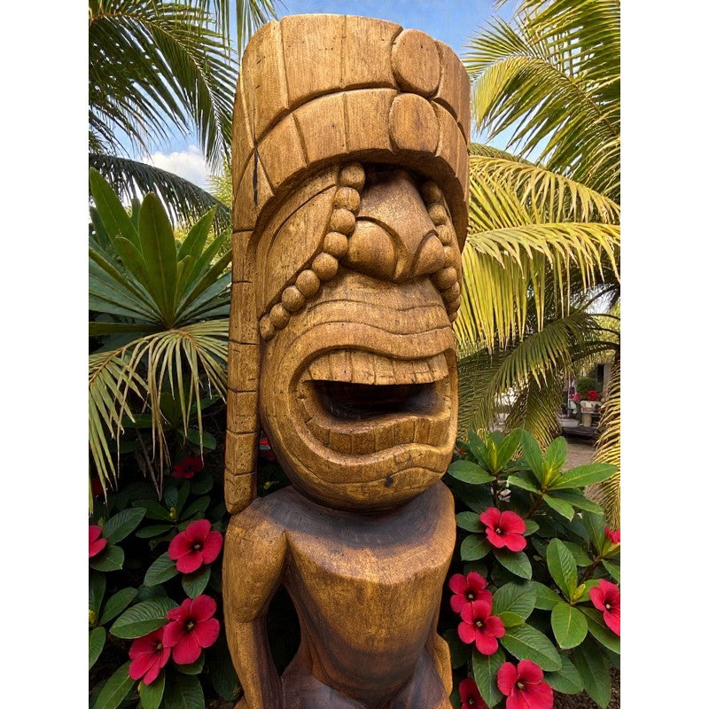 Wooden tiki statue with tropical plants and flowers in the background