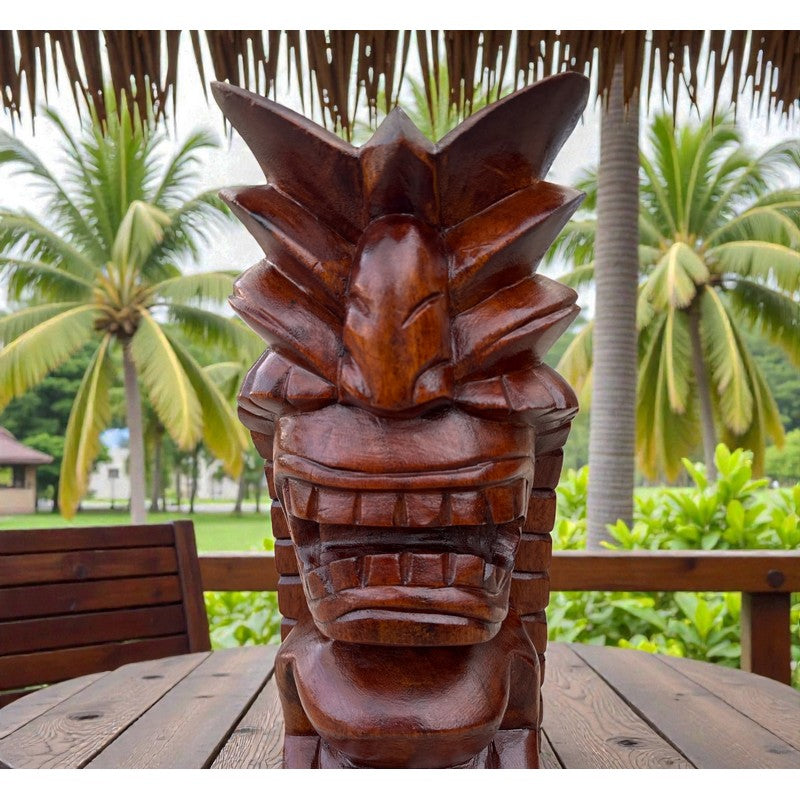 Wooden tiki statue on a table with palm trees in the background