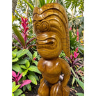 Wooden tiki statue in a garden setting with plants and flowers.