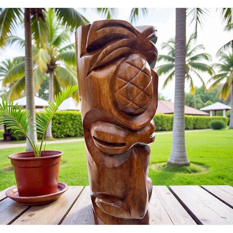 Wooden tiki mask with pineapple design on a wooden table outdoors with palm trees in the background