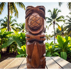 Wooden tiki statue on a wooden platform with tropical plants and palm trees in the background